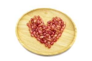 Fresh pomegranate heart shape on wooden plate isolated on white background photo