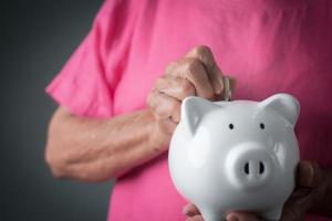 old senior woman putting coins into the piggy bank, photo