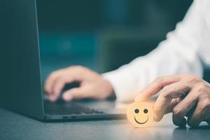 Young businessman holding a wooden block and sitting in front of a laptop, photo