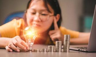 A young girl puts a light bulb on top of a pile of coins photo