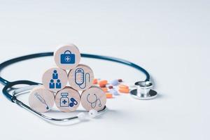 Wooden blocks stacked on top of each other, stethoscopes, pills are all placed on a white table, photo