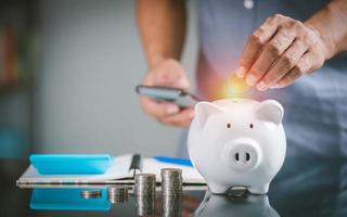 a businessman putting a coin in a white pig piggy bank , photo