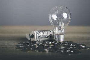 Light bulbs, dollar bills and stacks of coins all lay on the table, photo