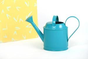 Light blue watering can isolated on white and yellow studio background photo