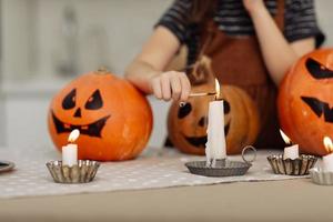 niña enciende una vela para halloween. niña en traje de bruja con calabaza tallada con una cara hecha por un niño. familia feliz preparándose para halloween. enfoque selectivo foto