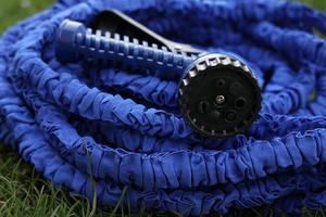 close up of watering hose lies on the grassy ground. blue rubber tube with device for spraying and watering plants in the garden. selective focus. photo