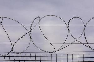 Barbed wire against the cloudy sky. Barbed wire fencing from the prison fence. The concept of captivity, slavery, prisoners, convicted. Prison, checkpoint, security territory, border, military base. photo