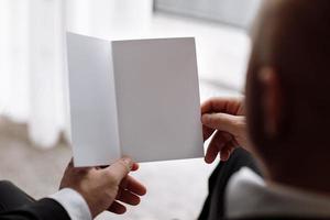 the groom holds an envelope with a letter from the bride. man is reading and sitting in the chair near the window. A letter for the groom. declaration of love. mock up place photo