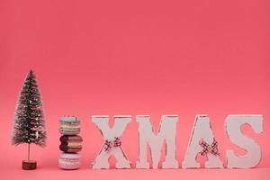 The wooden word xmas with colorful macaroons or macarons and christmas tree on pink background. Xmas decoration. New Year home decor photo