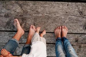 mamá, papá y bebé caminan descalzos sobre el puente de madera. feliz familia joven pasando tiempo juntos, corriendo afuera, yendo a la naturaleza, de vacaciones, al aire libre. el concepto de vacaciones en familia. copie el espacio foto