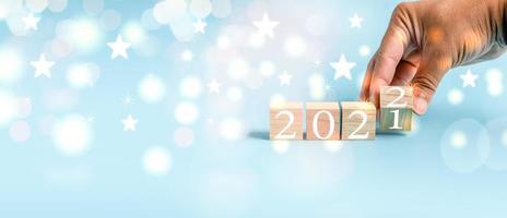 A person holding a wood cube and the wooden cube with the number changes 2021 to 2022. Concept Happy New Year has a bokeh and blue background. Closeup and copy space on left for design or text. photo