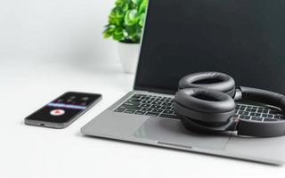 Headphones on a laptop. The concept of playing music with a smartphone and listening with wireless headphones on a white table. Close-up shot and selective focus. Spectrum and music notes on a screen photo