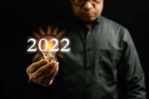 Close-up, A man holding a light bulb is the concept of the startup that drives global business. Bright lights give hope to small businesses. 2022 New Year concept, Copy space, Black Blurred background photo