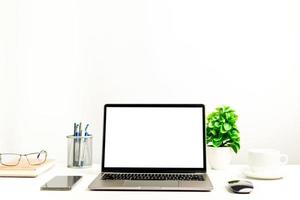 A working concept using technology, notebook, smartphones, devices. Blank white screen laptop on a white table in the office. Copy space on upper for design or text, Closeup, Gray, and blur background photo