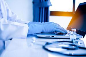 Doctor using a laptop for typing data, description into a server computer in hospital. Concept invented a cure, vaccine for coronavirus disease COVID-19. Closeup. Selective focus. Blurred background photo