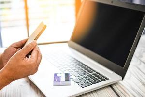 la mano de un hombre sostiene un teléfono inteligente para comprar en línea. los empresarios transfieren dinero con una aplicación móvil. una tarjeta de crédito o débito colocada en una computadora portátil. de cerca. enfoque selectivo. fondo borroso foto