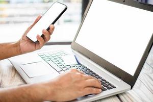 Men holding smartphones with white screen, blank. Businessmen transfer money via internet with smartphones to shop online,  payment. Laptops white screen on desk. Selective focus. Blurred background photo