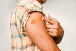 An orange plaster is attached to the man's arm. Concept for first aid after coronavirus COVID-19 vaccination, and professional, medical, needle, blood, cancer. Closeup, white blurred background photo