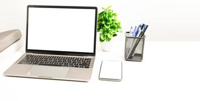 una computadora portátil de pantalla blanca en blanco sobre una mesa blanca en la oficina. teléfono inteligente de pantalla blanca en blanco. concepto de trabajo usando tecnología. copie el espacio a la derecha para el diseño o el texto, el primer plano, el gris y el fondo borroso