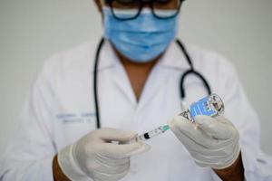 Doctors are experimenting with vaccination against the coronavirus. Scientists are using a syringe. A man wearing a mask holds a syringe and a vaccine bottle. Concept of the laboratory vaccine trial. photo