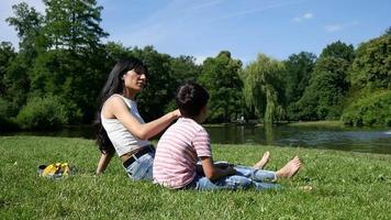 moeder en zoon zitten vredig samen aan het groene gras, familie in de buurt van het meer, zomerdag video