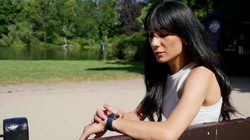 jovem morena usa relógio inteligente no pulso sentado no parque