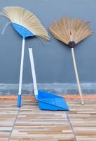 The double sweeping broom and the plastic dustpan are leaning against the sidewall of the house. photo