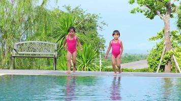 Happy little sisters are jumping into outdoor swimming pool in a tropical resort during family summer vacation. Kids learning to swim. Healthy Summer Activities for Kids. video