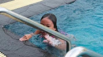 una niña feliz está nadando y jugando en la piscina al aire libre en un resort tropical durante las vacaciones familiares de verano. niña aprendiendo a bucear y nadar. actividades saludables de verano para niños. video