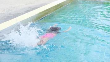 glad liten flicka simmar och leker i utomhuspoolen i en tropisk semesterort under familjens sommarsemester. flicka som lär sig dyka och simma. hälsosamma sommaraktiviteter för barn. video
