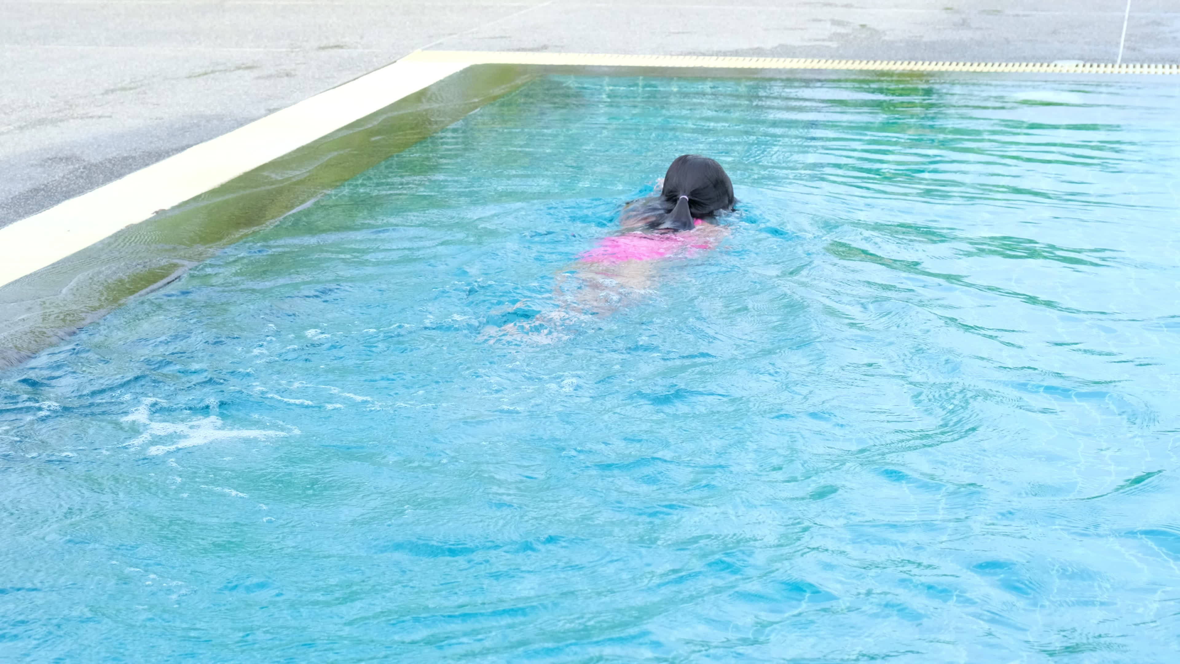 Happy little girl is swimming and playing in outdoor swimming pool in a