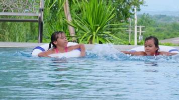 Happy little sisters with rubber ring in swimming pool. Kids play in outdoor swimming pool of tropical resort during family summer vacation. Kids learning to swim. Healthy Summer Activities for Kids. video