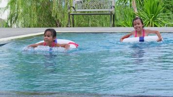 hermanitas felices con anillo de goma en la piscina. los niños juegan en la piscina al aire libre del complejo tropical durante las vacaciones familiares de verano. niños aprendiendo a nadar. actividades saludables de verano para niños. video