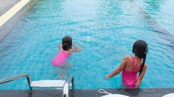 irmãzinhas felizes estão nadando e brincando na piscina ao ar livre em um resort tropical durante as férias de verão em família. crianças aprendendo a mergulhar e nadar. atividades de verão saudáveis para crianças.