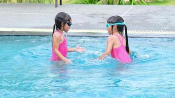 Happy little sisters are swimming and playing in outdoor swimming pool in a tropical resort during family summer vacation. Kids learning to dive and swim. Healthy Summer Activities for Kids. video