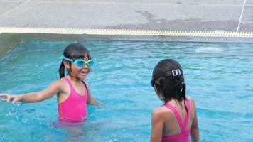 las hermanitas felices nadan y juegan en la piscina al aire libre en un complejo tropical durante las vacaciones familiares de verano. niños aprendiendo a bucear y nadar. actividades saludables de verano para niños. video