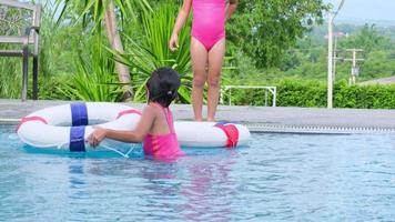 irmãzinhas felizes com anel de borracha estão pulando na piscina ao ar livre em um resort tropical durante as férias de verão em família. crianças aprendendo a nadar. atividades de verão saudáveis para crianças. video