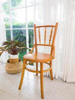 The vintage wooden chair is standing near a window decorated by the white curtain. photo