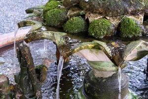 Closeup of the flowing water from the upper floor of the earthenware fountain with the many lichens. photo