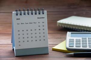 December 2023 white desk calendar on wooden table with notepad, calculator and pen background. Year end concept and copy space photo