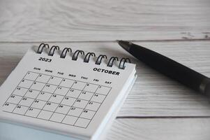 October 2023 white desk calendar with black pen on wooden table. photo