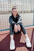 adorable mujer feliz vestida de negro sentada en la plaza del deporte a la luz del sol foto