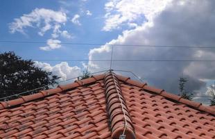 A roof with red shingles and a lightning conductor on it. photo