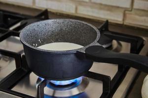 Cream is cooked in saucepan on gas stove to make cake photo