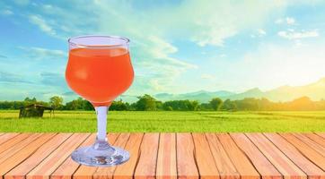 glass of orange juice beautiful wooden floor natural background green meadow and sky photo