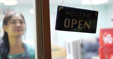 On a door store, a lady changes an open sign to a closed sign. video