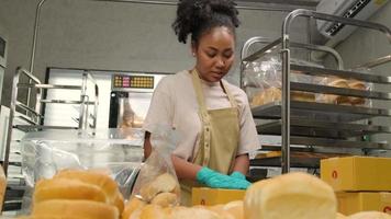 Bakery startup small business delivery. One African American female cook is packing handmade and fresh-baked bread and pastries in boxes and sending for online customer purchases in culinary kitchen.