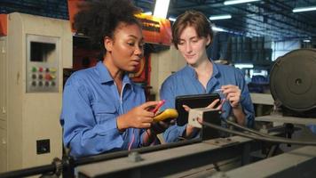 Two professional female engineer workers in safety uniforms work by inspecting machines' voltage current, checking, and maintaining at manufacturing factory, electric system service occupations. video