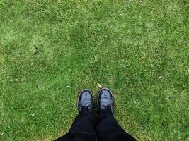 Two black shoes and legs on a grass surface - top view concept. photo