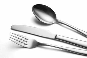 The metal shiny spoon, fork and knife on a white photo